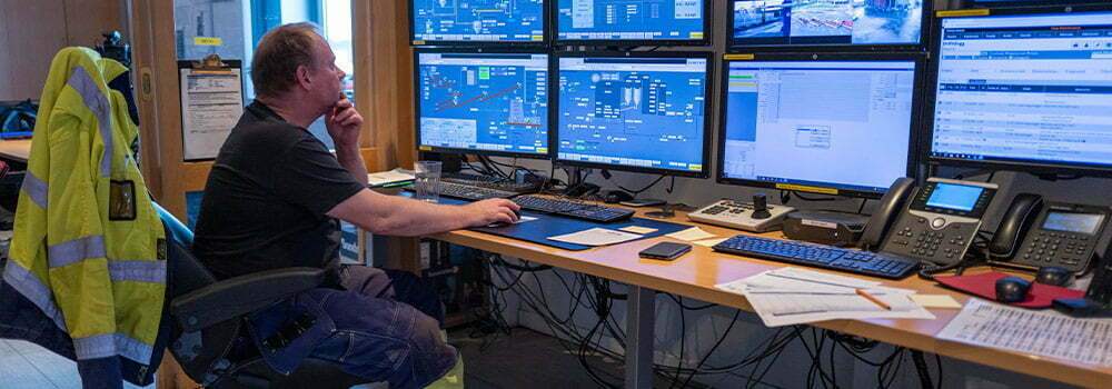 Bilde av en mann som sitter foran mange skjermer