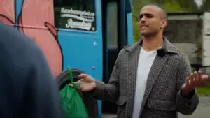 En person står foran en dekorert buss med en pose matavfall i hånda.