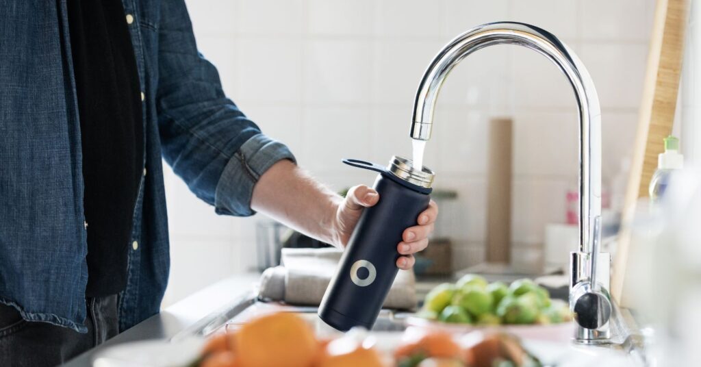 En vannflaske fylles med vann fra en vannkran.