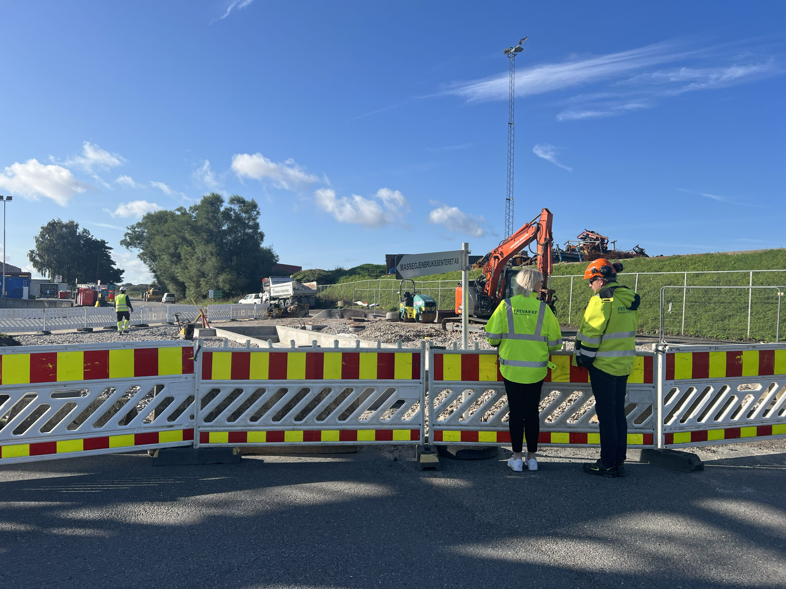 Bilde av en avsperret vei med to personer i lysegule vernejakker og hjelmer på seg som ser på arbeidet bak sperringene.