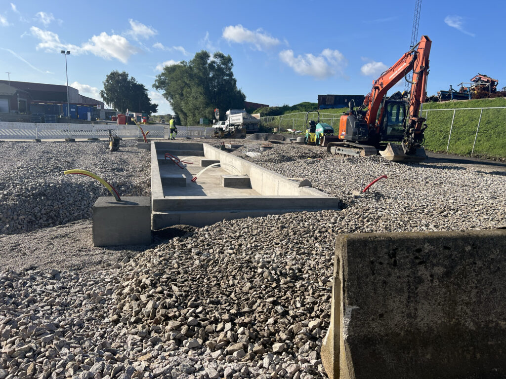 Bilde av anleggsarbeide ved vei. Betongkloss murt ned med pukk rundt. En oransje traktor står parkert på høyre side.
