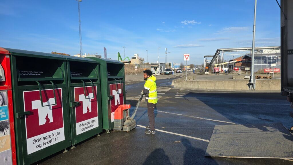 Avfallstasjon med en mann i verneutstyr som plasserer to nye tekstiltårn for tekstilgjennvinning på FREVAR.