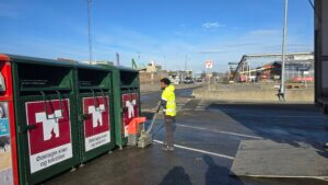 Avfallstasjon med en mann i verneutstyr som plasserer to nye tekstiltårn for tekstilgjennvinning på FREVAR.