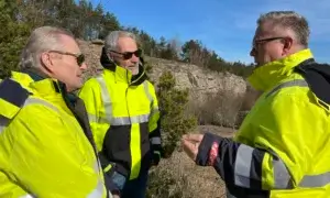 Tre personer i gule synlighetsklær på i kystlandskap, diskuterer mudder-løsning.
